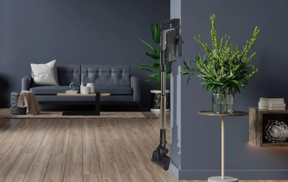 Tyčový vysavač Hisense HVC646630A Hi-Move VI Adapt InverterTech černý vysavač Hisense HVC646630A visí ve stanici na stěně v pokoji s tmavými stěnami a vybavením.. Vedle vysavače je rostlina.