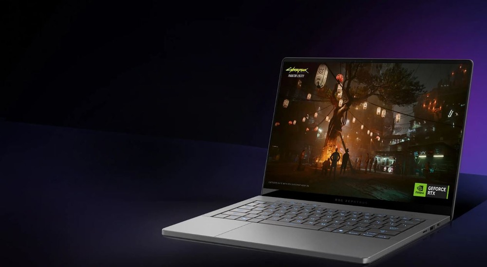 Notebook Asus ROG Zephyrus G14 bílý Elegantní šedý notebook otevřený na tmavém pozadí zobrazuje živou scému městského panoramatu hry Cyberpunk 2077.