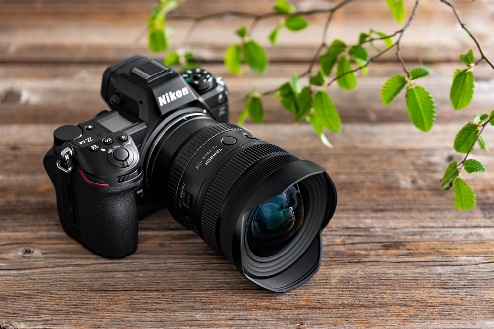 Objektiv Tamron 12-20 mm f/2.8 (Nikon) černý Fotoaparát Nikon s nasazeným objektivem Tamron 12–20 mm F/2.8 položený na dřevěném stole