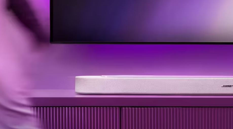 Soundbar Bose Lifestyle Ultra bílý Soundbar Bose Smart Ultra na televizním stolku pod TV s fialovým podsvícením.