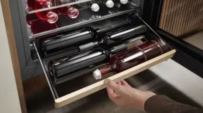 ruka vysunula polici na vino z lednice liebherr a na ní jsou uložene lahve vína.