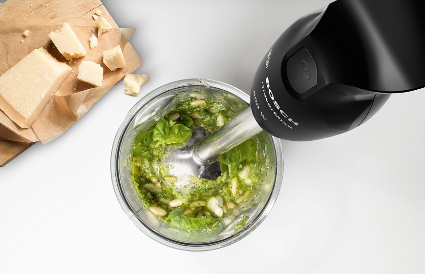 Pohled shora na tyčový mixér Bosch MSM2610B připravující zelené pesto, na stole je položen parmazán