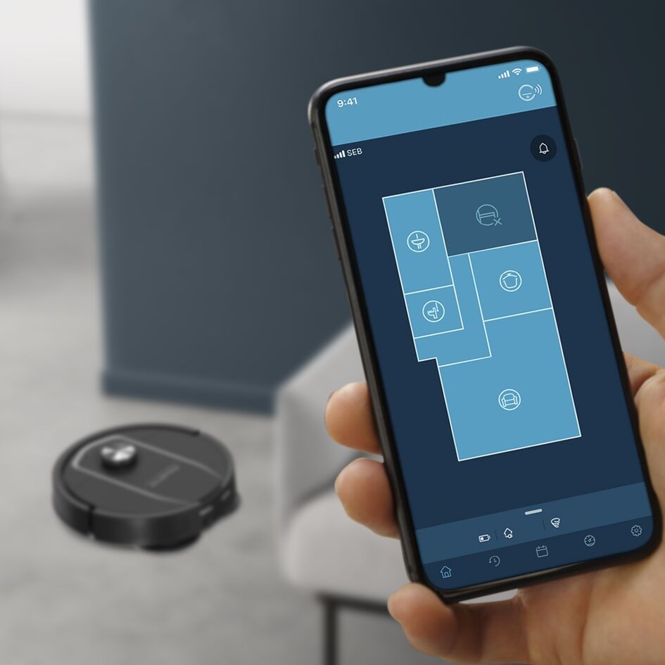 Robotický vysavač Rowenta X-Plorer S575 Max Wet & Dry 10000 PA RR95A5E0 černý Ruka držící smarphone se zapnutou mobilní aplikací Rowenta Robots a vysavač Rowenta RR95A5E0 na podlaze