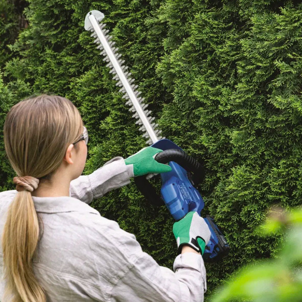 Žena tvaruje vysoké túje nůžkami Scheppach C-HT570-X s obouručním vedením