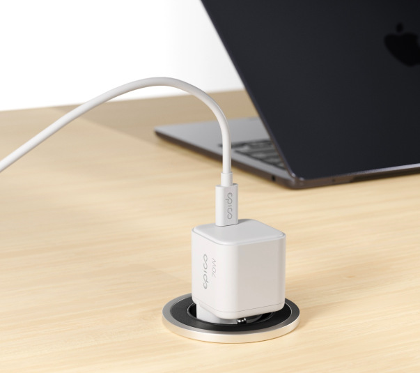 Napájecí adaptér Epico UltraBoost Micro AVS GaN 70 W zapojený ve stole při nabíjení notebooku