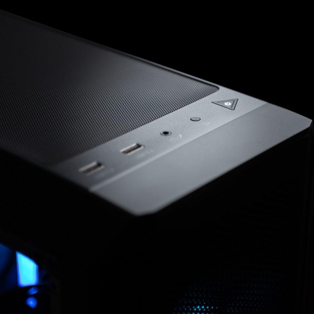 Detailní záběr na elegantní horní panel počítačové skříně za slabého osvětlení s USB porty, konektorem pro sluchátka a tlačítkem napájení s jemným modrým LED podsvícením.