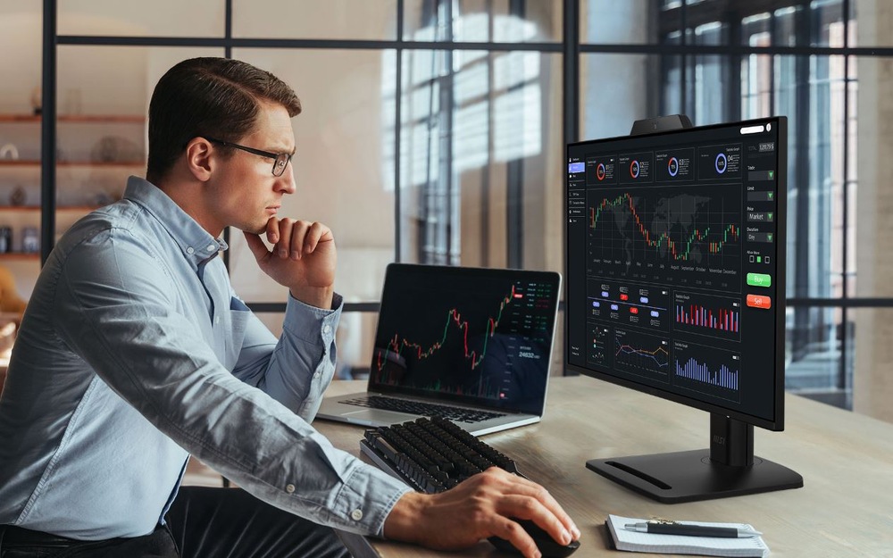 Monitor MSI PRO MP272PMG černý Muž pracující s monitorem MSI PRO MP272PMG a notebookem s finančními grafy