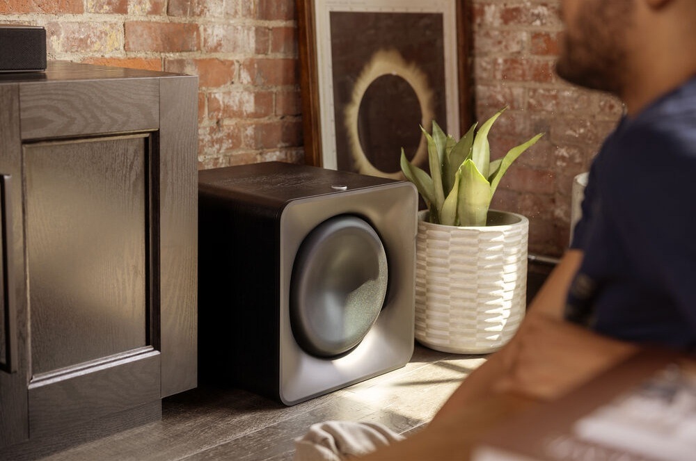 Subwoofer Klipsch Flexus SUB 200 černý Subwoofer Klipsch Flexus SUB 200 stojí na zemi mezi skříňkou a rostlinou v květináči, před ním sedí člověk