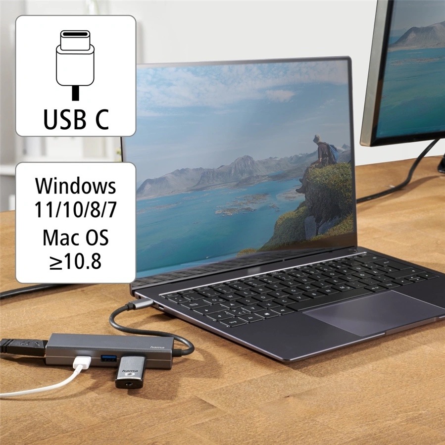 USB Hub Hama Multiport šedý Na obrázku je USB-C hub Hama použitý v praxi s notebookem na dřevěném stole. Hub leží vedle počítače, je do něj zapojený kabel a další zařízení, a krátkým kabelem je připojený k notebooku. Vlevo jsou informační ikonky s nápisem USB C a seznamem podporovaných systémů Windows 11/10/8/7 a Mac OS od verze 10.8. Fotka ukazuje běžné použití hubu pro rozšíření portů notebooku.