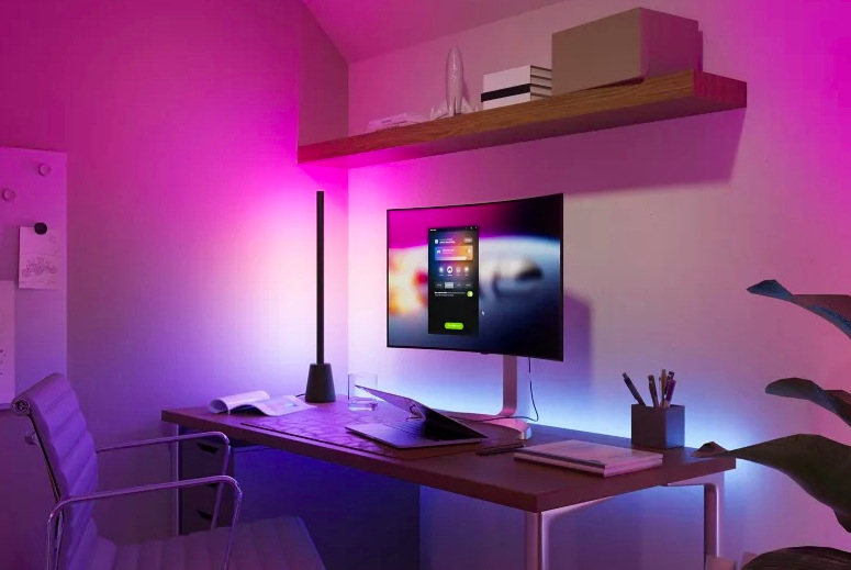 Stolní lampička Philips Hue Play nasvěcuje pracovní stůl a stěnu za monitorem barevnými přechody