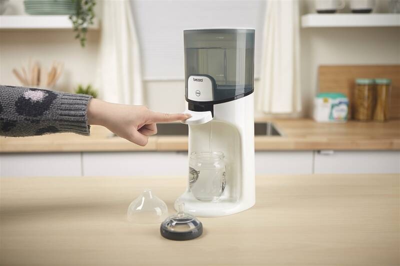 Ohřívač vody Baby Brezza Instant Warmer White bílý Pod dávkovač vody je umístěna kojenecká lahvička a ruka dospělé osoby stlačila páčku, aby se nadávkovalo potřebné množství vody.