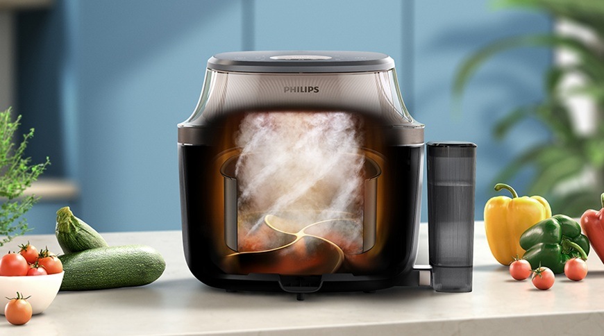 Horkovzdušná fritéza Philips NA547/07 s grafickým znázorněním proudění horkého vzduchu a páry uvnitř během přípravy. Vedle spotřebiče je umístěná nádoba na vodu a na kuchyňské lince jsou čerstvé suroviny, jako cuketa, papriky a rajčata.