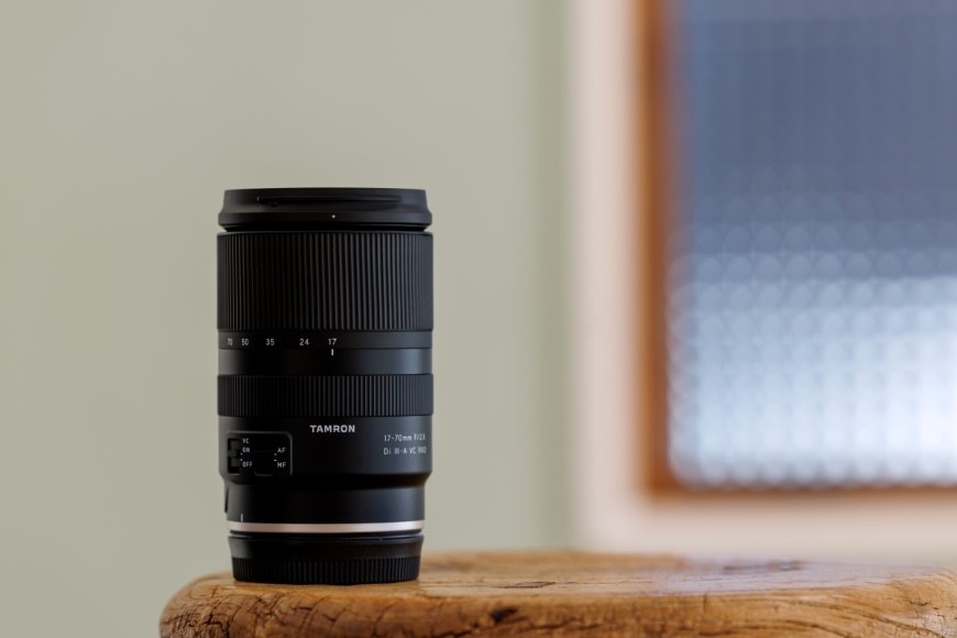 Objektiv Tamron 17-70 mm f/2.8 Di III-a RXD (Canon) černý Zátiší s objektivem Tamron 17–70 mm f/2.8 Di III-a RXD stojícím na stole