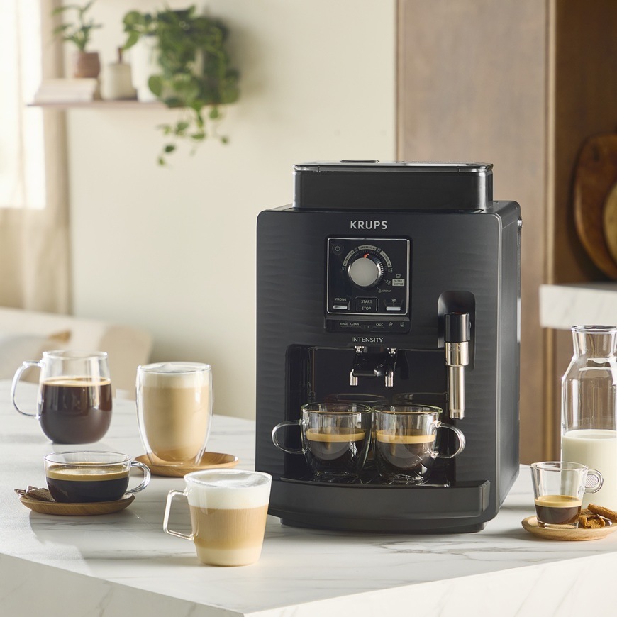 Automatický kávovar Krups EA5008E0 Intensity Up Black připravuje dva šálky kávy najednou. Okolo kávovaru jsou připravené nejrůznější druhy káv.