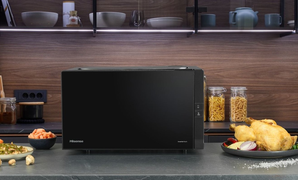 Mikrovlnná trouba Hisense H25MOBS4HGI Invertor černá Mikrovlnná trouba Hisense H25MOBS4HGI na kuchynske lince hnede kuchyně. Vedle jsou talire s jidlem