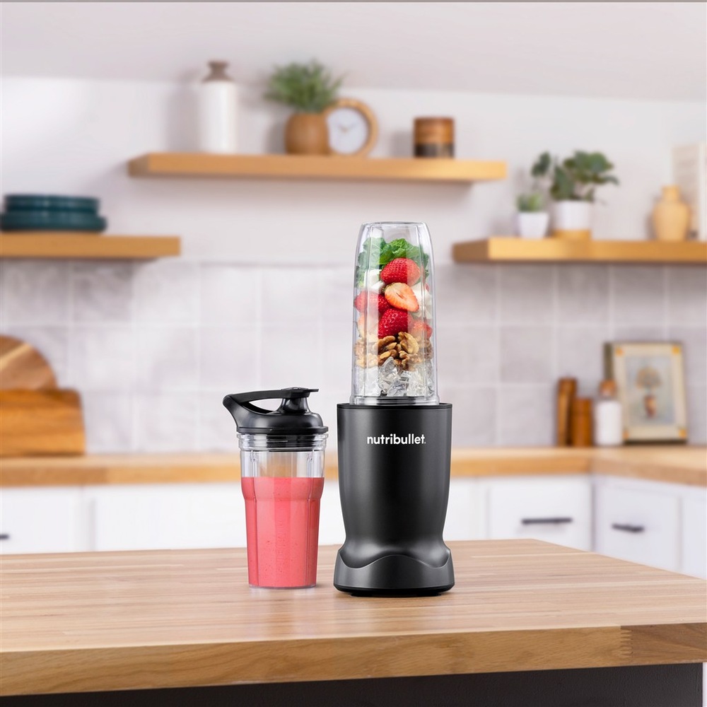 Mixér NutriBullet na kuchyňském pultu vedle přenosného kelímku s růžovým smoothie.