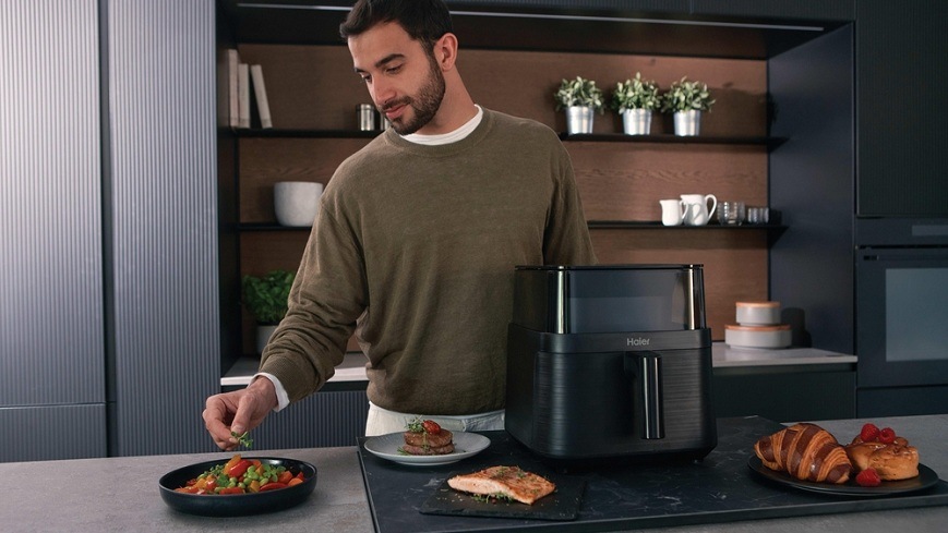 Fritéza horkovzdušná Haier I-Master Series 3 HAF3AFW 011 černá muž dochucuje jeden z hotových pokrmů, které se nacházejí v okolí horkovzdušné fritézy Haier HAF3AFW 011