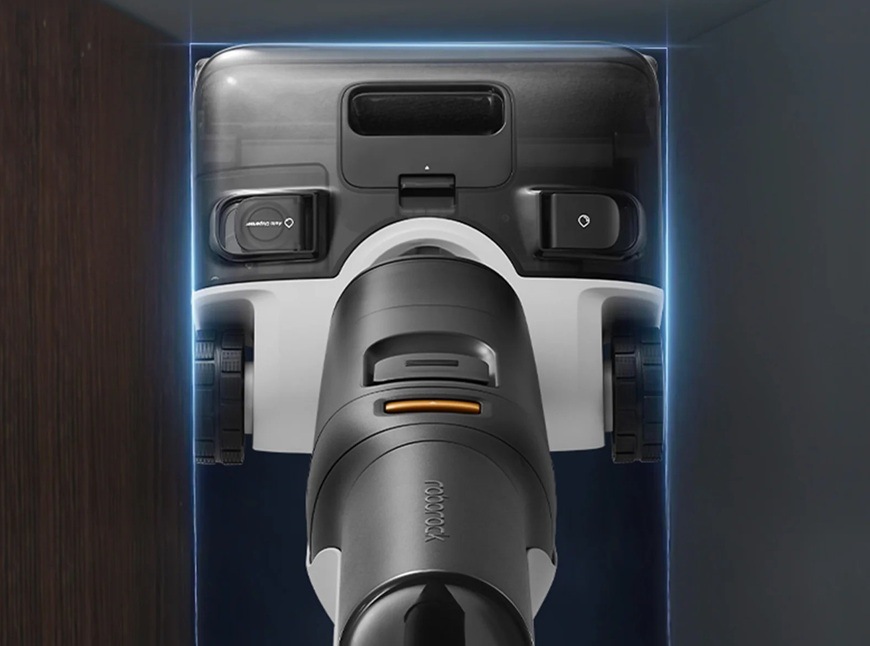 Tyčový vysavač Roborock F25 ACE Combo černý Horní pohled na tyčový vysavač Roborock F25 ACE Combo přisátý k podlaze v úzkém prostoru ukazující kompaktní konstrukci a přesné vedení při úklidu kolem stěn a nábytku.