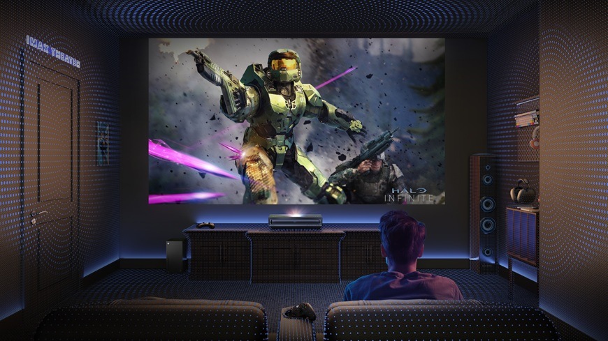Muž sedí na gauči v domácím kino sále a před sebou má zapnutý projektor Hisense PX3-PRO, na kterém hraje akční hru.