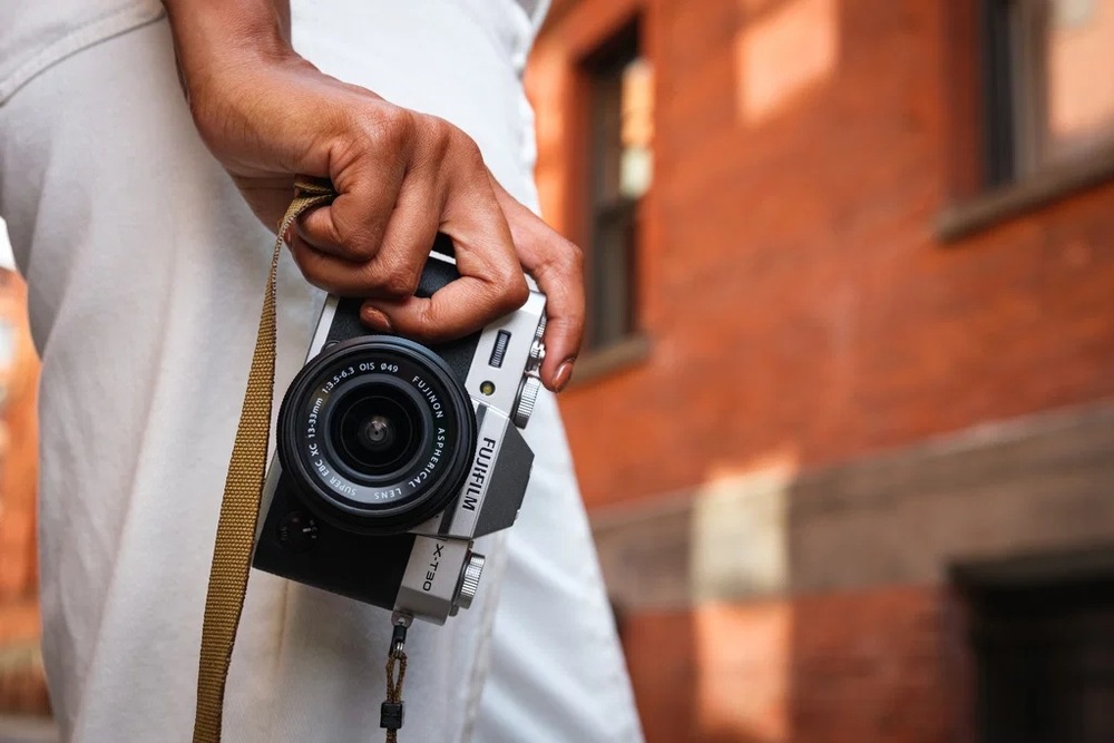 Detal jdoucí osoby s kompaktním fotoaparátem Fujifilm X-T30 III v ruce