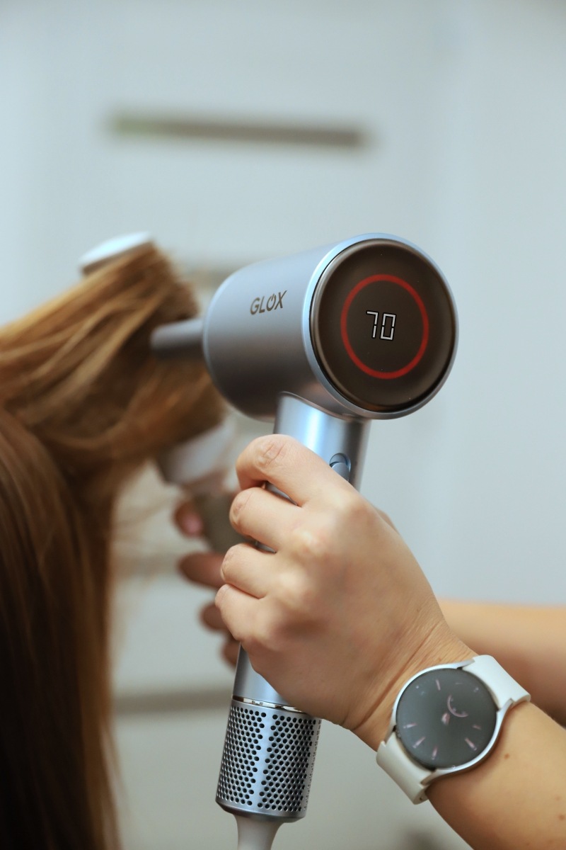 Fén GLOX GLOXD3S stříbrný Kadeřník upravuje vlasový pramen pomocí fénu GLOX s digitálním displejem zobrazujícím teplotu 70 °C.