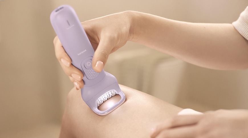 Epilátor Philips BRE728/00 ve fialové barvě přiložený k pokožce nohy, detail epilační hlavice s osvětlením během odstraňování chloupků.