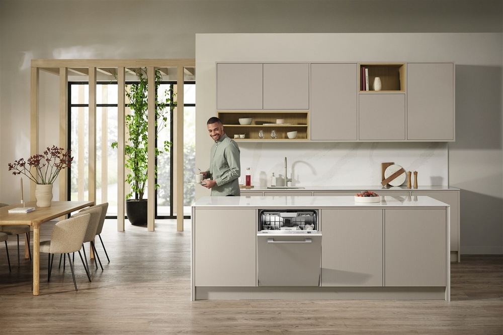 Myčka nádobí Miele G 5856 SCVi XXL Active Plus Vestavná myčka Miele s pootevřenými dvířky v kuchyni, za ostrůvkem s myčkou stojí muž a dívá se směrem k myčce