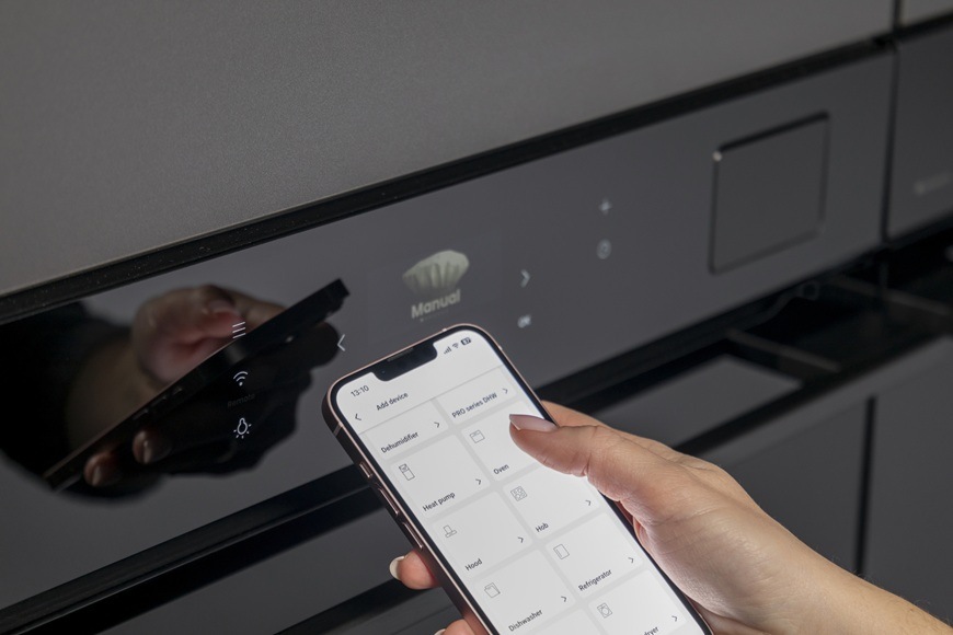 Trouba Hisense BAS614P8B černá Žena v ruce drží chytrý mobilní telefon. V něm má otevřenou aplikaci ConnectLife pro dálkové ovládání trouby.