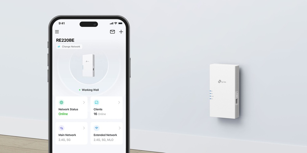Smartphone zobrazuje aplikaci pro správu sítě, která ukazuje stav „Funguje dobře“ s 16 připojenými klienty. Nedaleko je do zásuvky zapojeno bílé zařízení pro rozšíření sítě, které symbolizuje moderní a efektivní technologické vybavení.