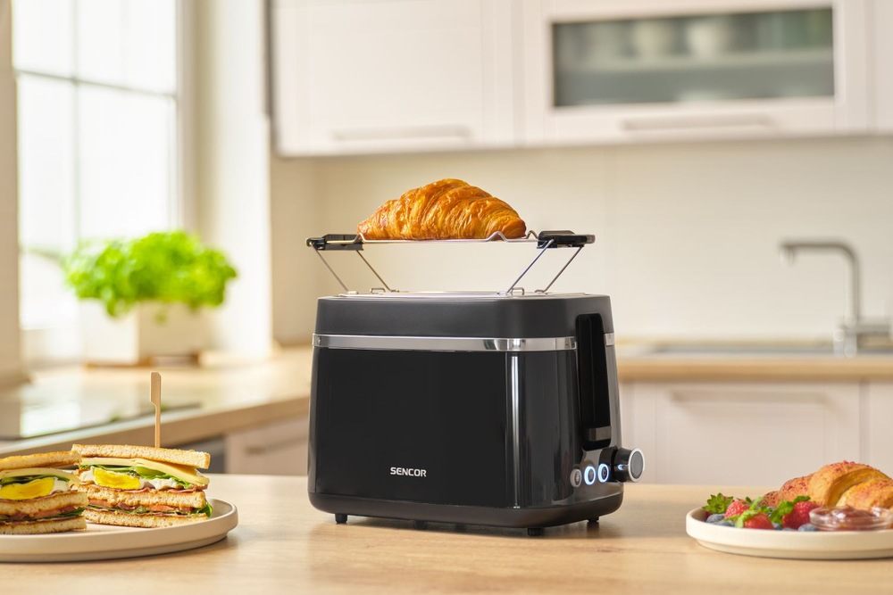 Croissant ohřívaný na mřížce topinkovače Sencor STS 2710BK, vedle kterého leží hotové toasty a další snídaně.