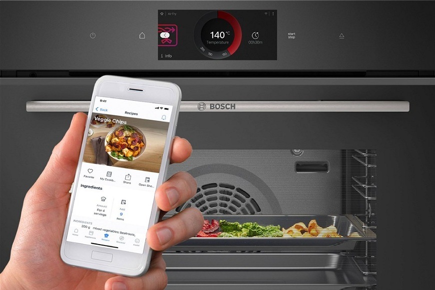Ruka s mobilem a aplikací Home Connect, v pozadí vestavná trouba Bosch