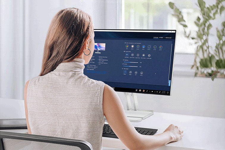 Monitor Lenovo L24-4C šedý Žena pracuje u stolu s notebookem a monitorem, na kterém jsou zobrazeny tabulky a grafy. Světlá místnost s velkými okny, rostlinami a klidnou, soustředěnou atmosférou.