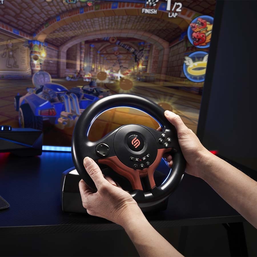 Volant SUPERDRIVE SV250 SP Edition Red červený Ruce svírající herní volant před záběrem ze hry Rocket League. Prostředí vyvolává vzrušení a ponoření se do děje.