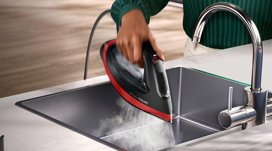 Osoba čistí napařovací žehličku Philips DST6130/40 6000 Series v kuchyňském dřezu.