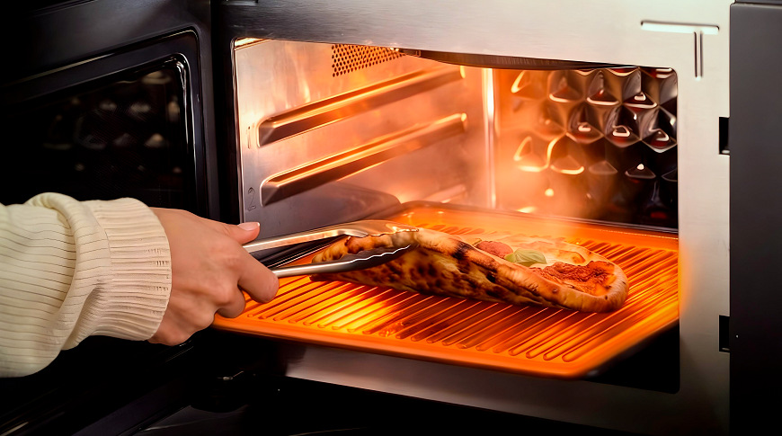 ruka vytahuje pizzu z mikrovlnné trouby a ukazuje, že je zespoda upečená do křupava.