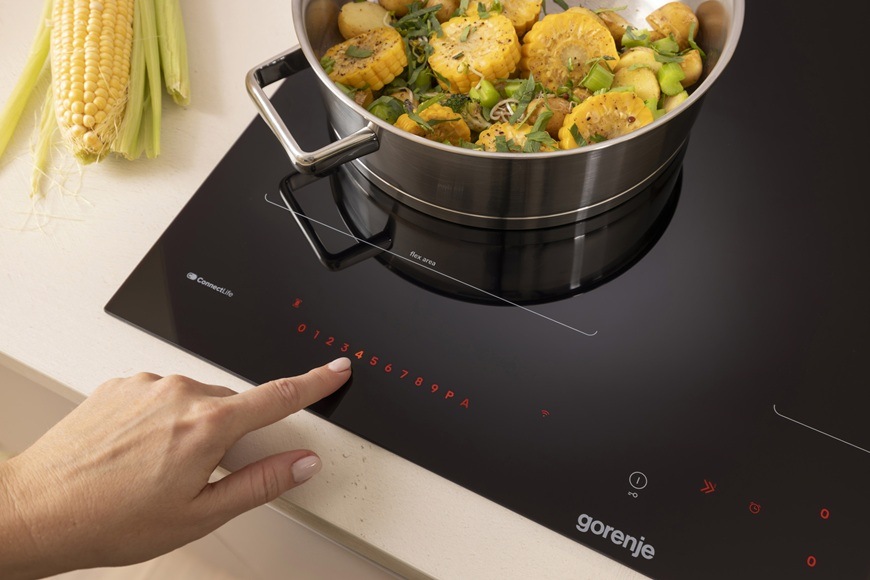 Indukční varná deska Gorenje G800 GI6443BSCWF černá Na indukční varné desce Gorenje GI6443BSCWF je položen hrnec a v něm jsou nakrájené kukuřicové lusky a pórek. Žena zvyšuje výkon varné zóny.