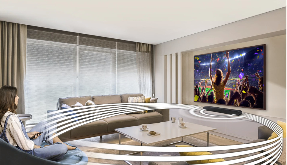 Soundbar Samsung HW-S50B černý Soundbar Samsung HW-S50B je na skříňce po televizí Samsung v obývacím pokoji, proti televizi sedí žena sledující přehrávaný obsah, ze soundbaru vycházejí bílé kruhy, které znázorňují šíření prostorového zvuku