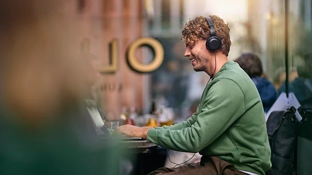 Sluchátka Philips TAH2100BK/00 černá Smějící se muž pracující na notebooku má na hlavě sluchátka Philips