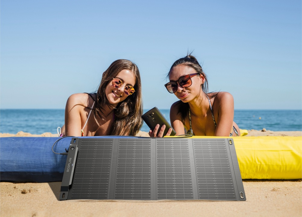 Dvě dívky na pláži s panelem EcoFlow a mobilem v ruce