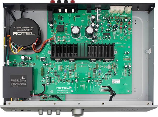 Interiér audio zesilovače Rotel zobrazující zelenou desku s různými elektronickými součástkami a zapojením.