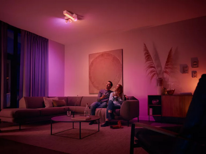 Pár v obývacím pokoji s barevným osvětlením Philips Hue v růžovo-fialových tónech.