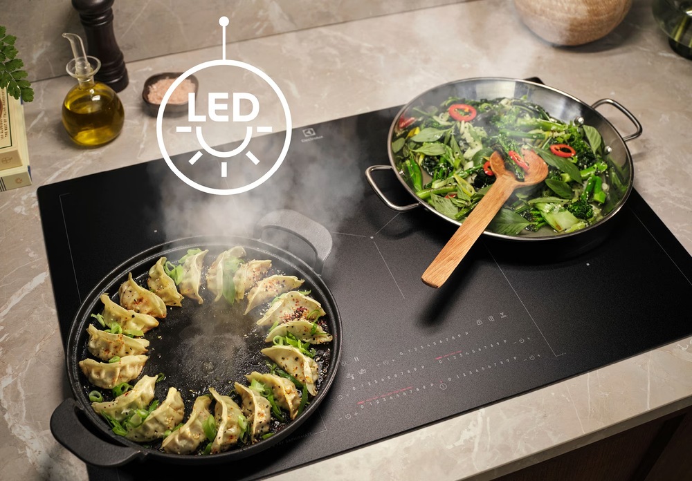 Odsavač par Electrolux série 500 LFC519X nerez Varná deska Electrolux s pánví raviol a zeleniny. Nad deskou symbol pro LED osvětlení.
