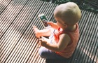 Batole sedící na verandě a držící v ruce mobilní telefon se spuštěnou fotoaplikací