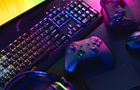 Na stole leží před monitorem klávesnice, 2 gamepady a myš