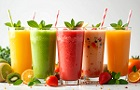 Sklenice s ovocnym smoothie v ruzných barevných provedeních. Vedle sklenic se válí ovoce.