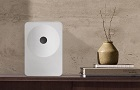 Reproduktor Samsung Music Studio 7 v bílé barvě stojí na dřevěném stolku vedle dekorativní vázy.